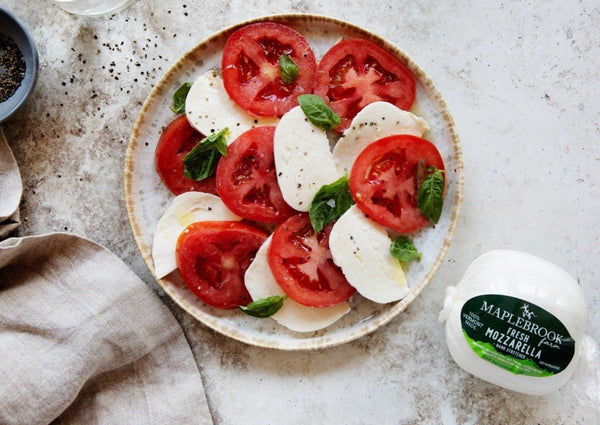 Maplebrook Farm Fresh Mozzarella Cheese shown in package with plate of tomatoes and sliced cheese