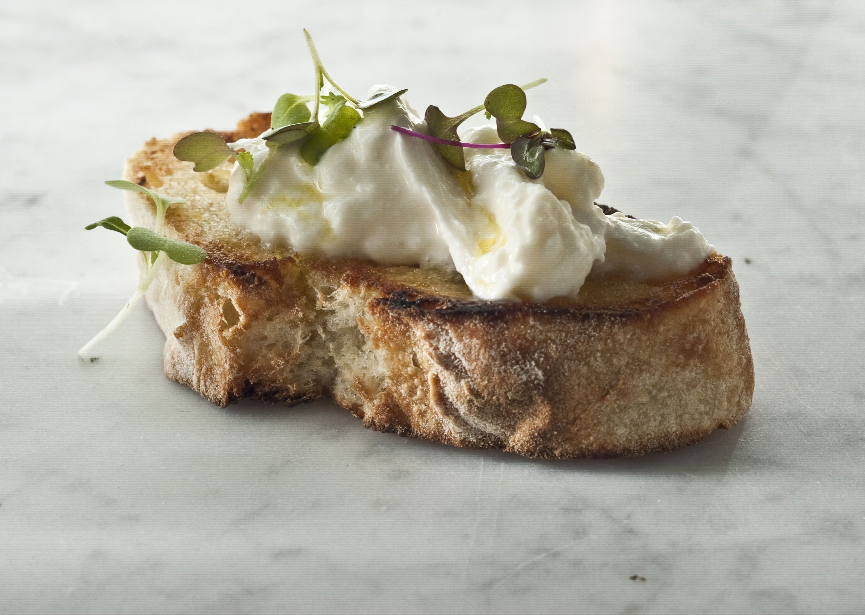 Stracciatella spooned over toasted bread